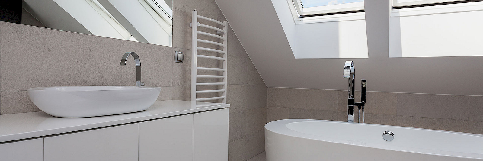 A bright and airy loft bathroom with a modern bathtub, enhanced by natural light streaming through two Velux windows offering a beautiful view of the clear blue sky. Perfect for loft conversion ideas and inspiration.