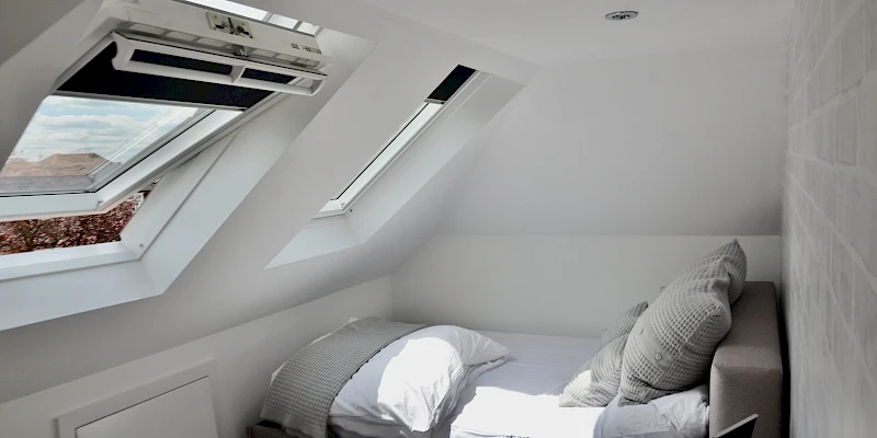 Stylish loft conversion bedroom featuring a spacious and cozy design. Highlighted by sloping ceilings and skylights that bring in natural light, this serene retreat combines modern aesthetics with practical use of space.