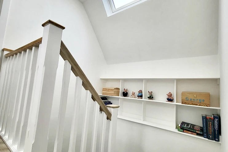 Elegant white wooden staircase leading up to a loft conversion, with a bright and inviting hallway. The clean lines and light tones create a modern, airy feel, complementing the contemporary design of the space and enhancing the flow of natural light throughout the home.