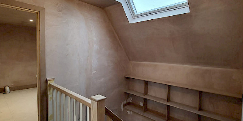 A beautifully designed Velux loft conversion featuring a raw, unfinished plaster interior. The photo showcases the clean, open space with the characteristic Velux windows allowing natural light to flood the room, highlighting the exposed plasterwork on the walls and ceiling.