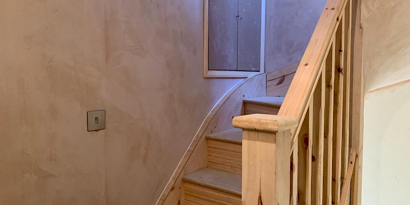 This photo showcases a stunning loft conversion with a raw wooden staircase and freshly plastered walls, offering a perfect blend of natural materials and modern design.